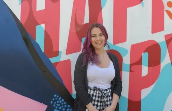 Marisa Layes standing in front of the "Happy" mural at Griffith College Dublin