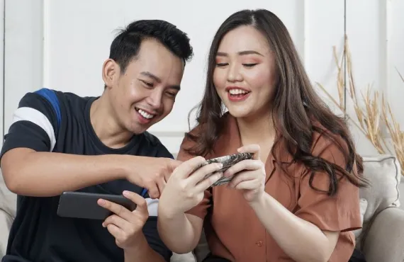 A man and woman sitting on a couch inside, looking at a phone screen together