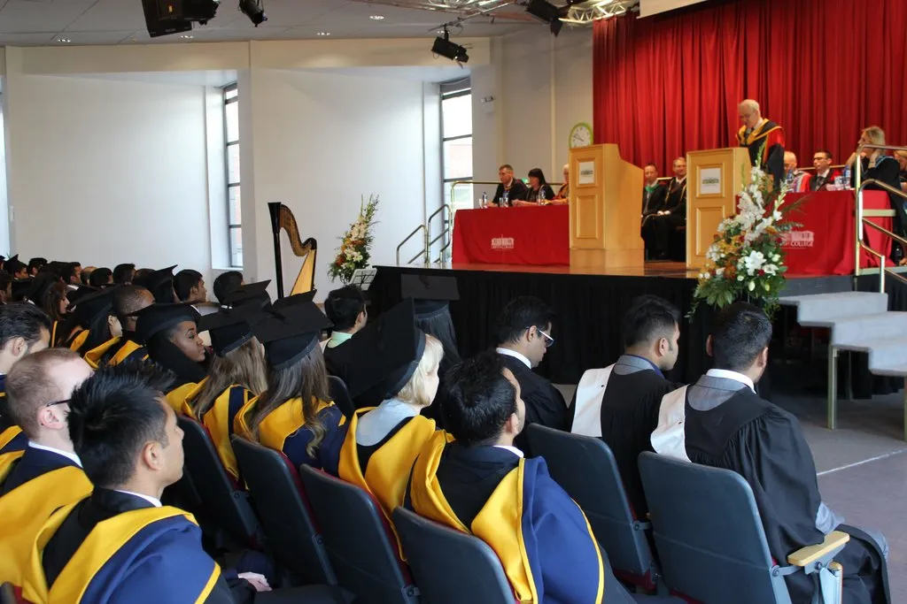 Griffith College graduation ceremony Several rows of graduates in cap & gowns look up at a raised dais with a speaker at a Griffith College graduation ceremony
