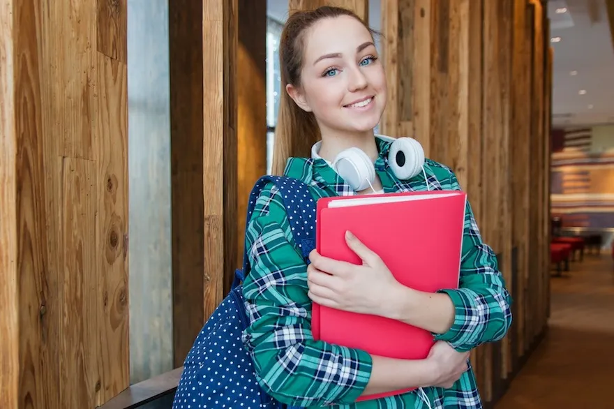 Griffith College learn and earn offers school leavers the chance to continue their education while starting their careers. A young woman standing in the hallway, holding school books and smiling at the camera