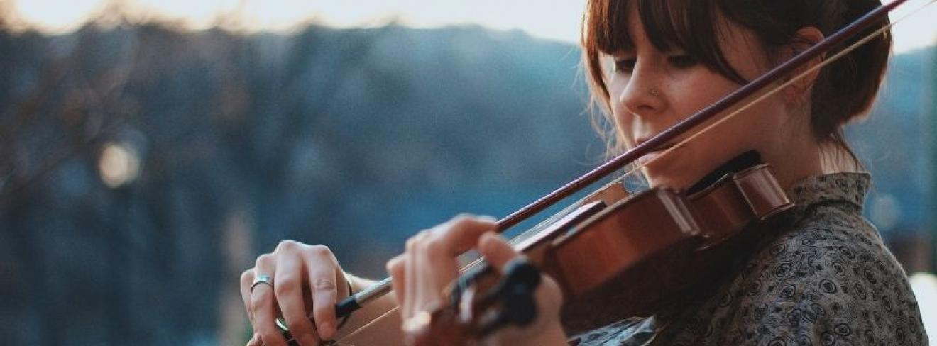 Rate your ability with the LSMD A young woman playing violin on a balcony with trees in the background