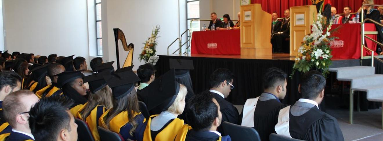 Griffith College graduation ceremony Several rows of graduates in cap & gowns look up at a raised dais with a speaker at a Griffith College graduation ceremony